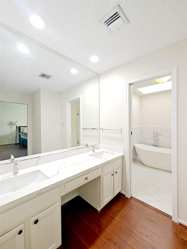 ensuite bathroom featuring a freestanding tub, visible vents, and a sink