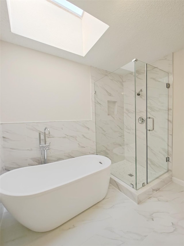 bathroom featuring a textured ceiling, a skylight, a freestanding bath, marble finish floor, and a marble finish shower