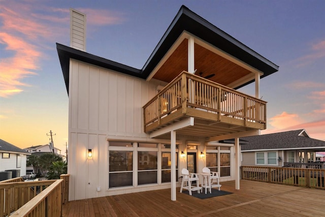 back of property at dusk with a balcony, a chimney, board and batten siding, and a wooden deck