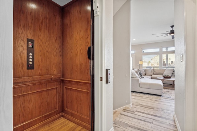 hall featuring baseboards, a textured wall, light wood-style floors, and elevator