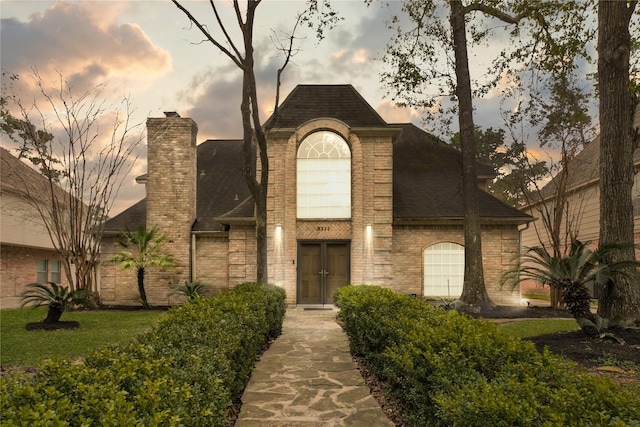 french provincial home with a chimney, brick siding, and a shingled roof