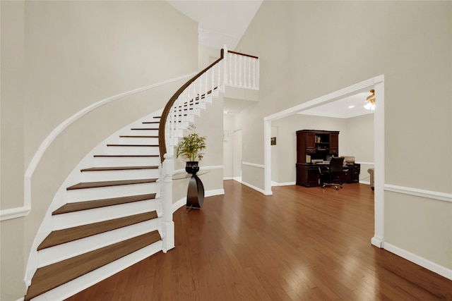 foyer entrance with stairs, a high ceiling, baseboards, and wood finished floors