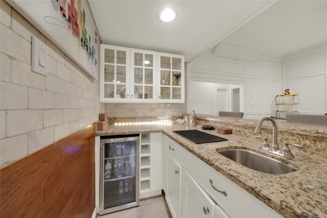 kitchen with light stone counters, light tile patterned flooring, a sink, wine cooler, and glass insert cabinets