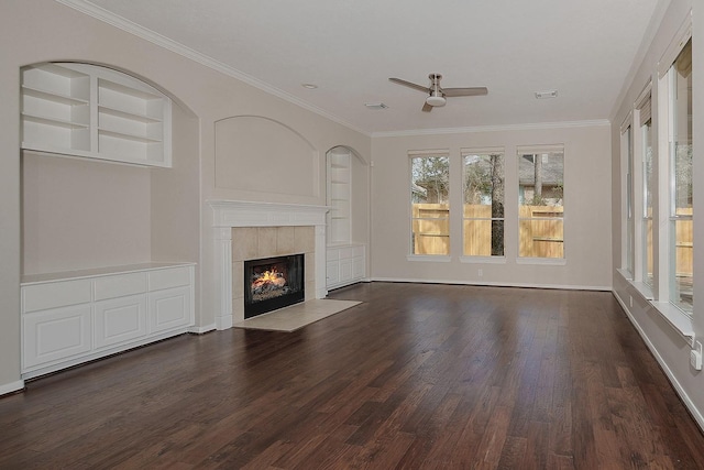 unfurnished living room featuring crown molding, built in shelves, dark wood-type flooring, and a tiled fireplace