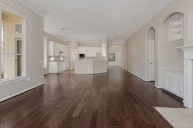 unfurnished living room featuring baseboards, arched walkways, dark wood finished floors, and crown molding