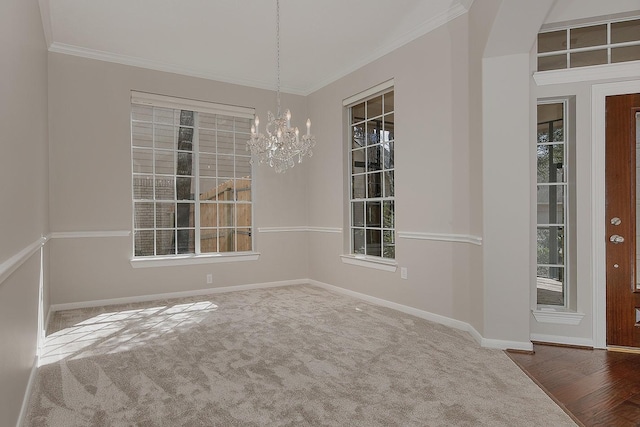 carpeted empty room featuring a chandelier, ornamental molding, and baseboards