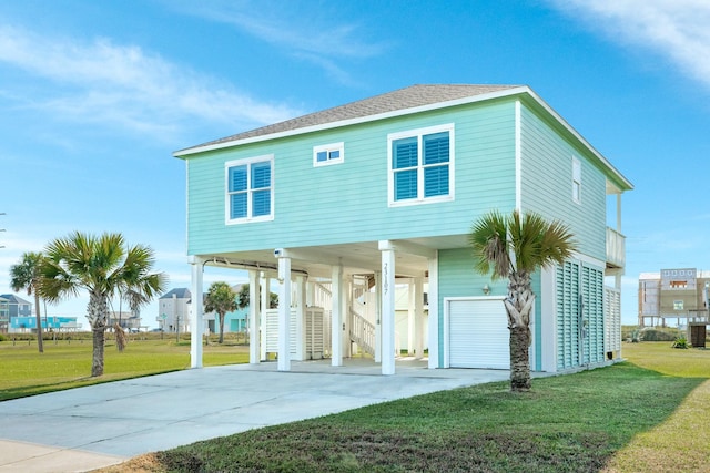 beach home featuring a shingled roof, concrete driveway, stairway, a front yard, and a carport