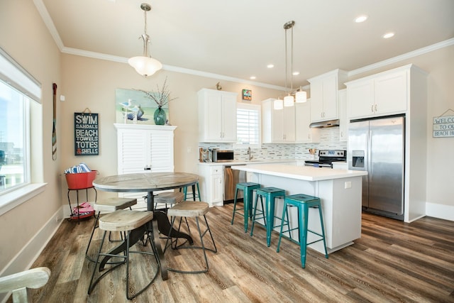 kitchen with under cabinet range hood, stainless steel appliances, ornamental molding, a center island, and tasteful backsplash