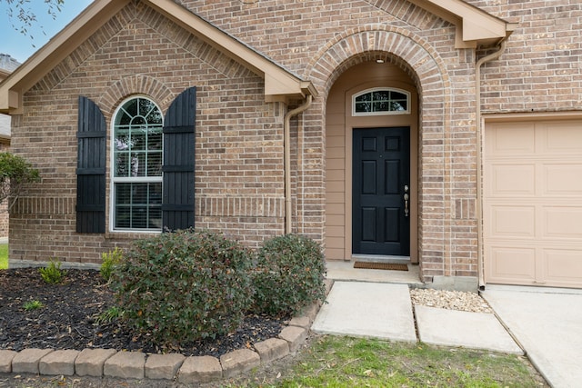 entrance to property featuring a garage and brick siding