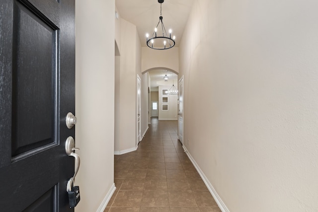 hall featuring an inviting chandelier, tile patterned flooring, arched walkways, and baseboards