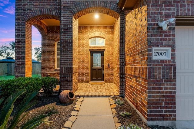 view of exterior entry with a garage and brick siding