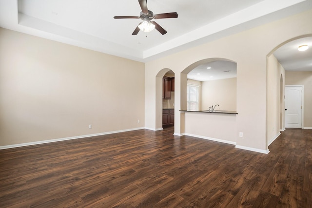 unfurnished room featuring a sink, a ceiling fan, baseboards, dark wood-style floors, and a raised ceiling