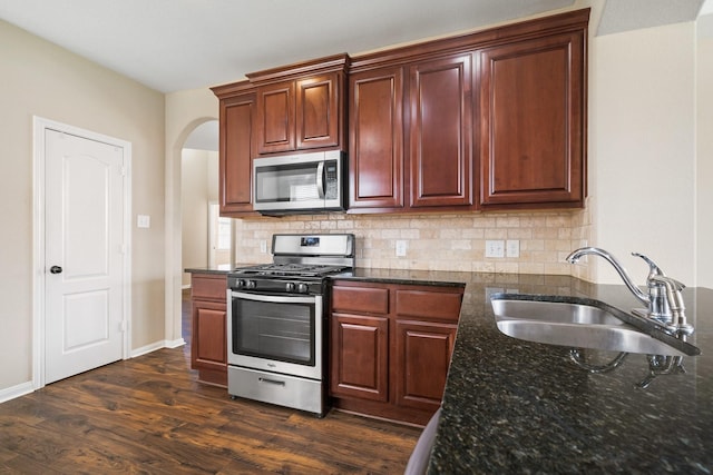 kitchen with appliances with stainless steel finishes, a sink, dark wood finished floors, and decorative backsplash