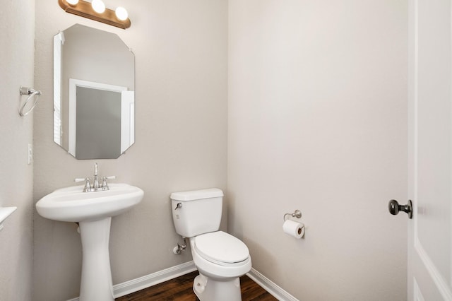 half bath with baseboards, a sink, toilet, and wood finished floors