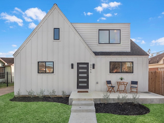 modern inspired farmhouse featuring roof with shingles, board and batten siding, a front yard, and fence