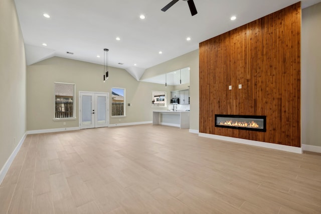 unfurnished living room with ceiling fan, high vaulted ceiling, recessed lighting, light wood-type flooring, and a glass covered fireplace