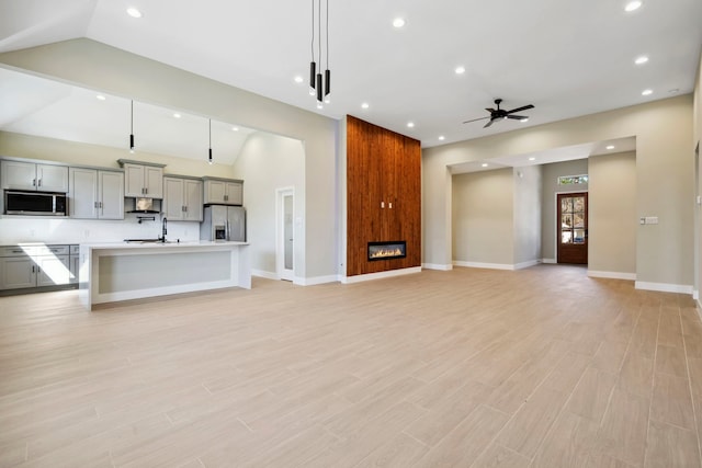 unfurnished living room with light wood finished floors, a ceiling fan, vaulted ceiling, a fireplace, and recessed lighting