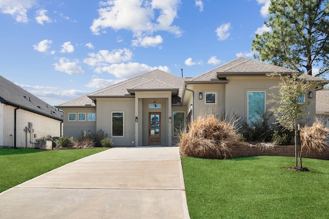 prairie-style home featuring roof with shingles, a front lawn, and stucco siding