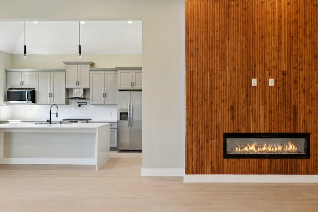 kitchen with gray cabinetry, stainless steel appliances, a sink, backsplash, and range hood