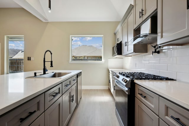 kitchen with lofted ceiling, under cabinet range hood, stainless steel appliances, and a sink