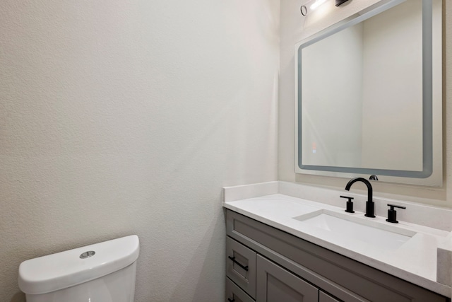 bathroom with toilet, a textured wall, and vanity