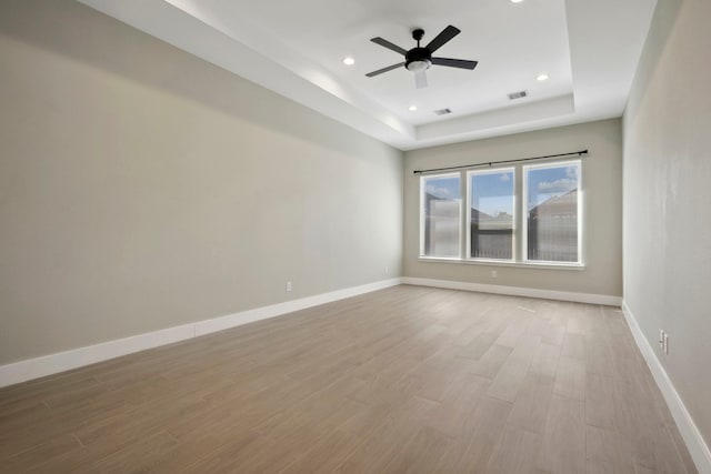 spare room featuring a raised ceiling, visible vents, baseboards, and wood finished floors