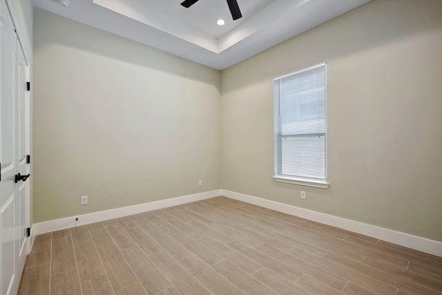 unfurnished room featuring ceiling fan, recessed lighting, light wood-style floors, baseboards, and a tray ceiling