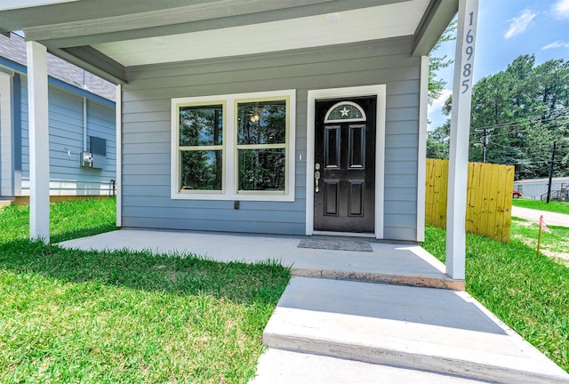 doorway to property with covered porch, a yard, and fence