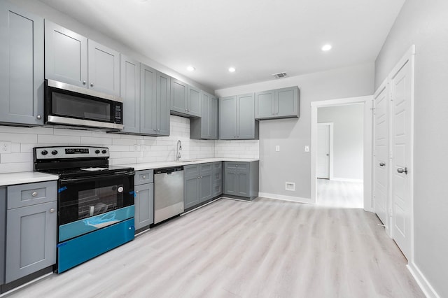 kitchen featuring visible vents, light wood-style flooring, a sink, stainless steel appliances, and backsplash