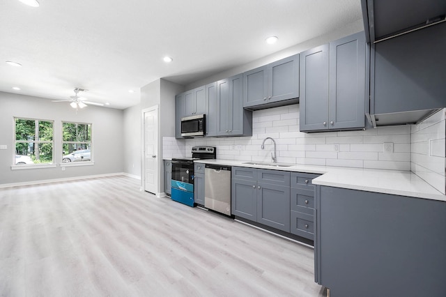 kitchen with light wood finished floors, light countertops, decorative backsplash, appliances with stainless steel finishes, and a sink