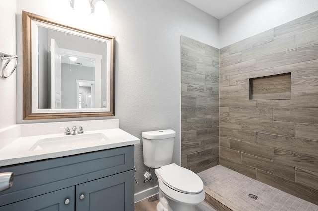 bathroom featuring toilet, a tile shower, and vanity