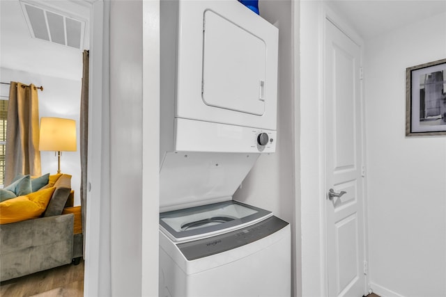 laundry room featuring laundry area, visible vents, stacked washing maching and dryer, and wood finished floors