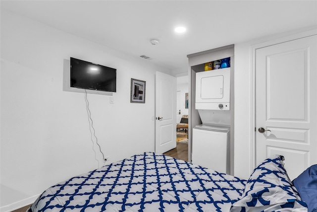 bedroom featuring visible vents, stacked washer / drying machine, and wood finished floors