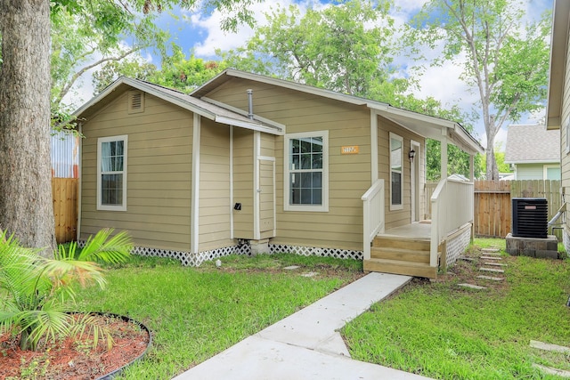 view of front of property with central AC, fence, and a front lawn