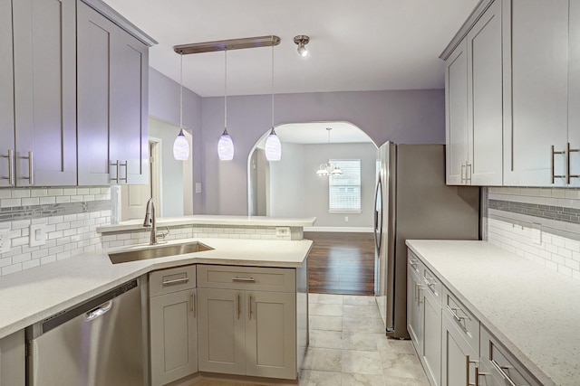 kitchen featuring arched walkways, a peninsula, hanging light fixtures, stainless steel dishwasher, and a sink