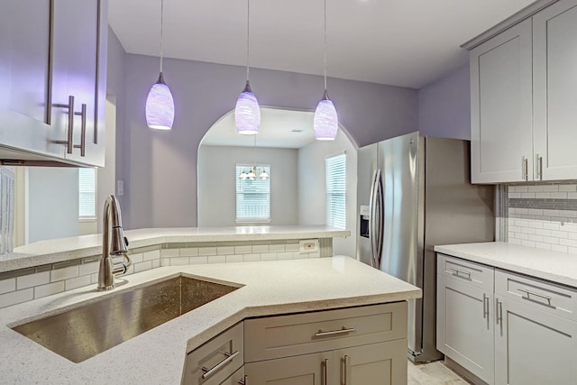 kitchen featuring light stone counters, decorative light fixtures, a sink, and backsplash