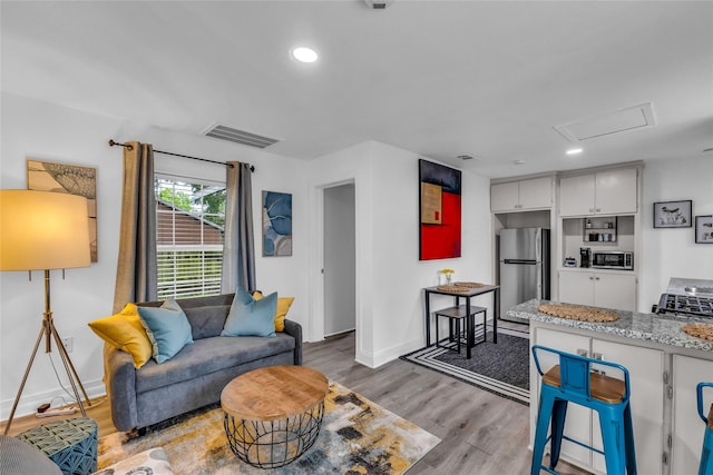 living room featuring attic access, visible vents, baseboards, light wood-style floors, and recessed lighting