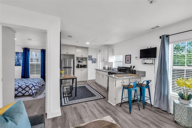 kitchen with freestanding refrigerator, white cabinetry, visible vents, and a kitchen breakfast bar