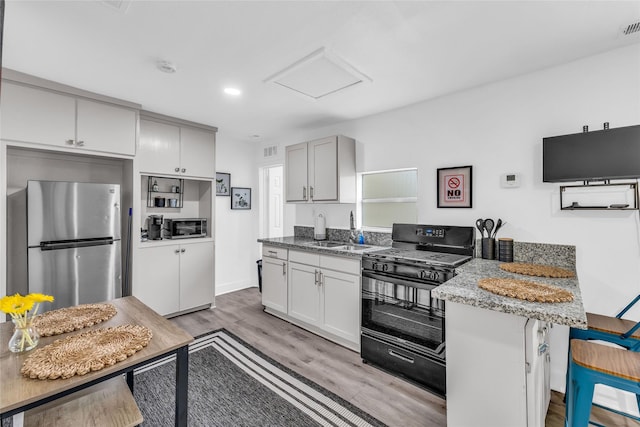 kitchen with light wood finished floors, black gas range oven, freestanding refrigerator, a sink, and a peninsula