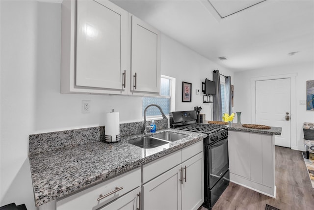 kitchen featuring light stone counters, a peninsula, a sink, white cabinets, and black gas range oven