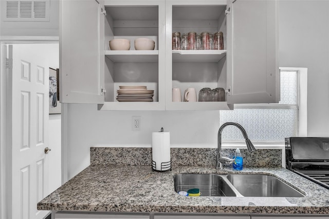 details featuring open shelves, a sink, visible vents, and light stone countertops