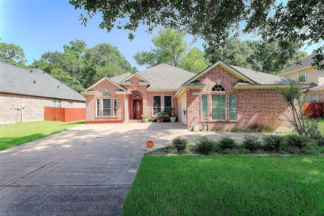 single story home with brick siding, fence, driveway, roof with shingles, and a front yard