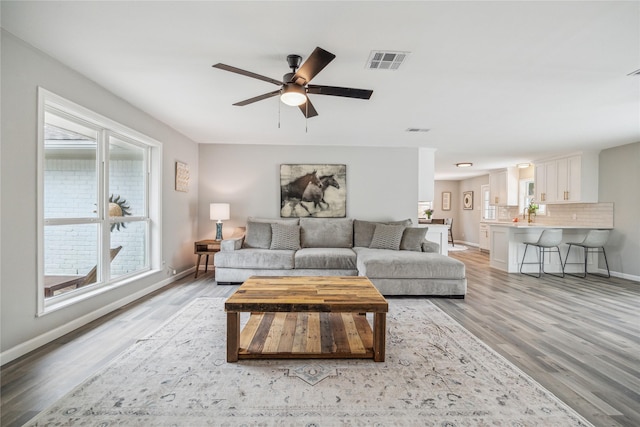 living room featuring a ceiling fan, light wood-type flooring, visible vents, and baseboards