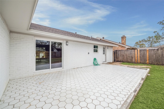 rear view of house featuring a patio area, brick siding, fence, and roof with shingles