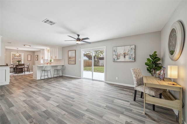 interior space featuring ceiling fan with notable chandelier, wood finished floors, visible vents, and baseboards