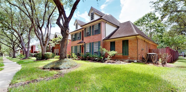 view of front facade featuring a shingled roof, fence, a front lawn, and brick siding