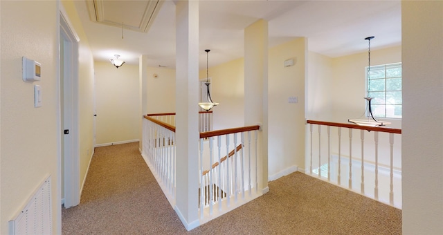 corridor with attic access, baseboards, visible vents, carpet flooring, and an upstairs landing