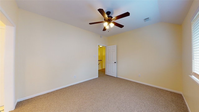 empty room featuring lofted ceiling, visible vents, a ceiling fan, light carpet, and baseboards