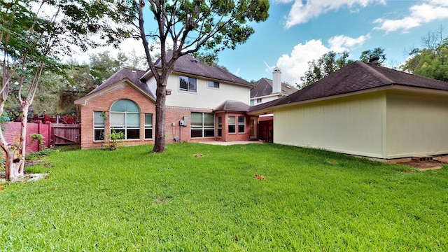 rear view of house with brick siding, fence, and a yard