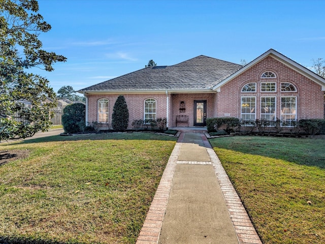 view of front of home featuring a front yard, brick siding, and roof with shingles